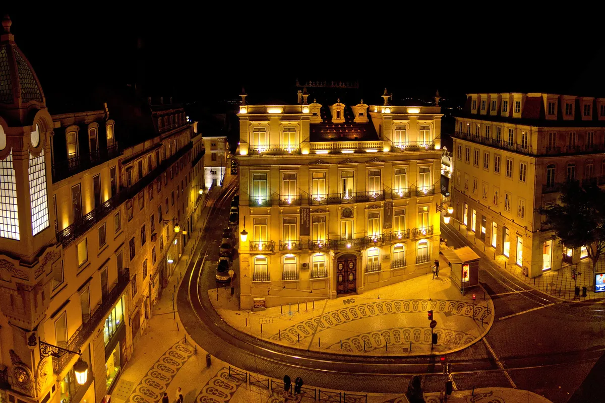 The Largo do Chiado square at night with lit yellow facades and a clock tower on the left.